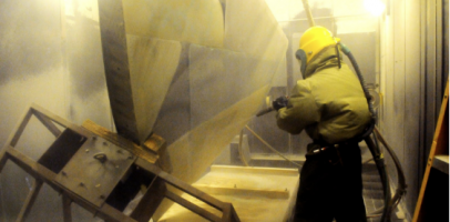 an image of a worker in a blast room cleaning a metal part