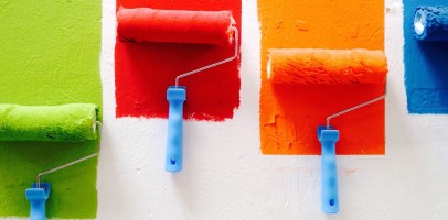 four paint rollers coating a while wall with different primary colours